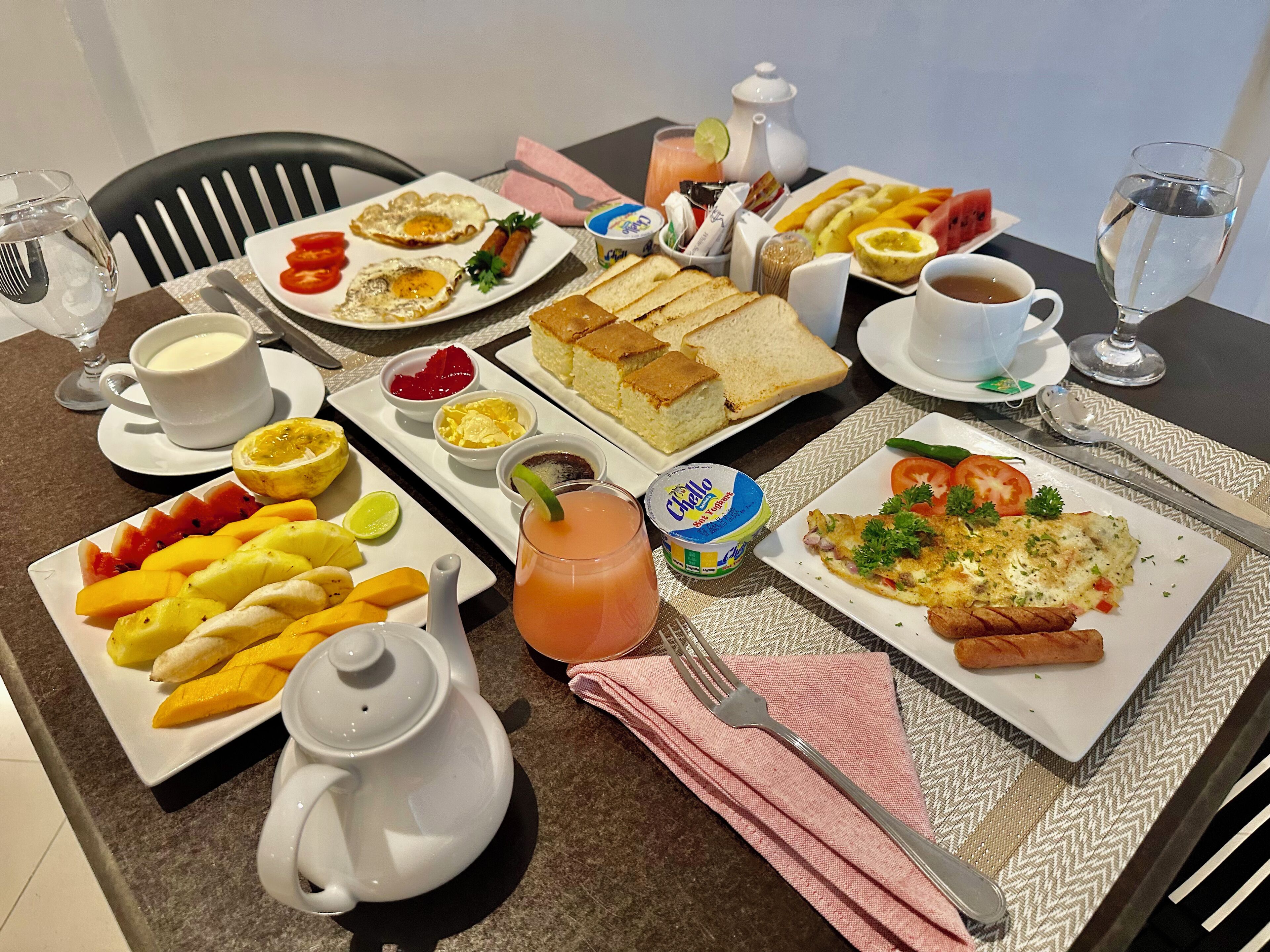 A breakfast table with various dishes including eggs, toast, fruit, and beverages.