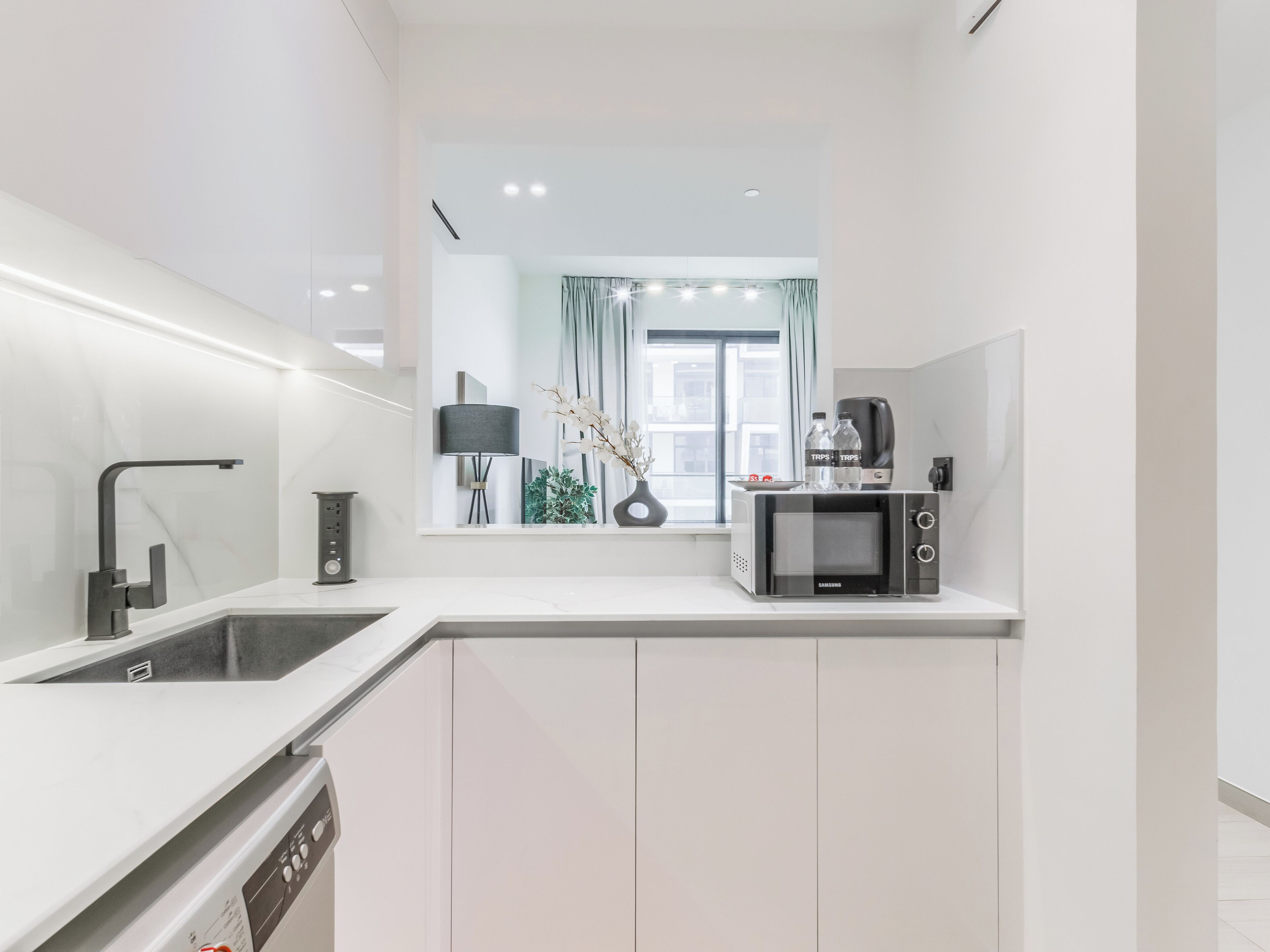 Una cucina moderna con mobili bianchi, lavastoviglie integrata, forno a microonde e macchina da caffè.