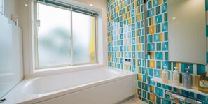 A bathroom with a bathtub, a window, and a tiled wall with a geometric pattern. - Ocean Villa Tokunoshima (Tokunoshima)