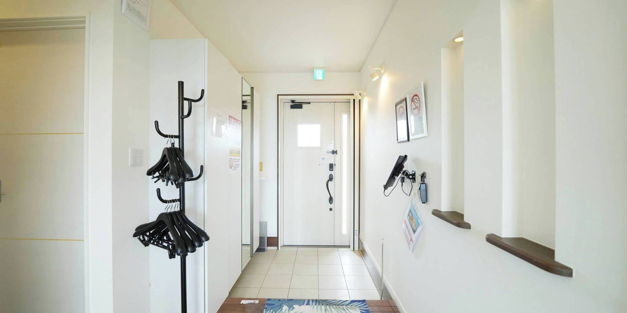 Un couloir avec un porte-manteau, une porte dotée d’une poignée et un luminaire fixé au mur.