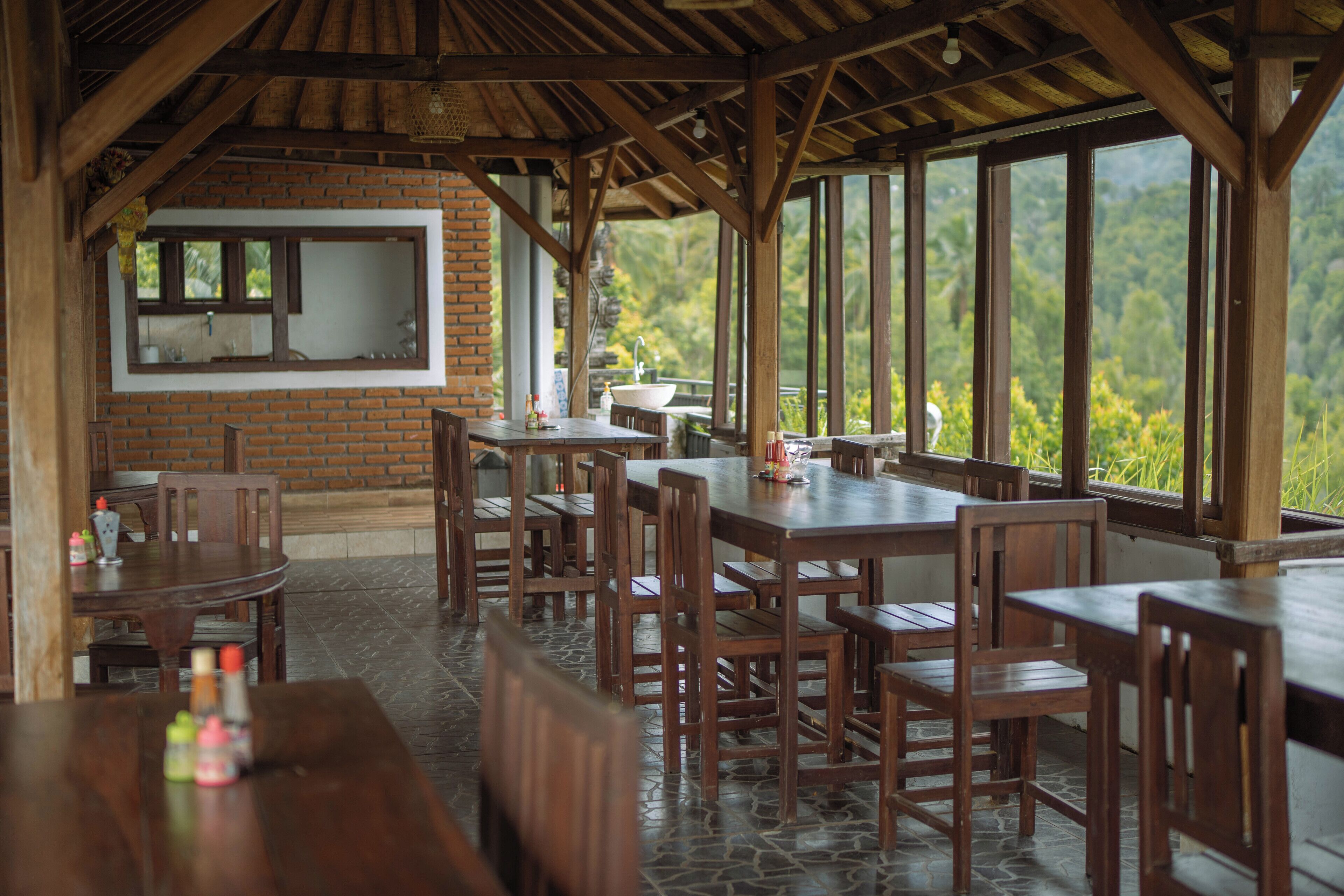 A restaurant with wooden tables and chairs, a brick wall, and large windows overlooking a lush landscape.