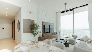 Un salon moderne comprenant un coin repas, un grand téléviseur à écran plat fixé sur un mur à texture, et une vue sur la ville grâce à de grandes fenêtres.