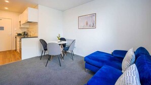 Een ruimtelijk ingerichte leefruimte met kitchenette, een eethoek met ronde tafel en stoelen, en een blauwe bank.
