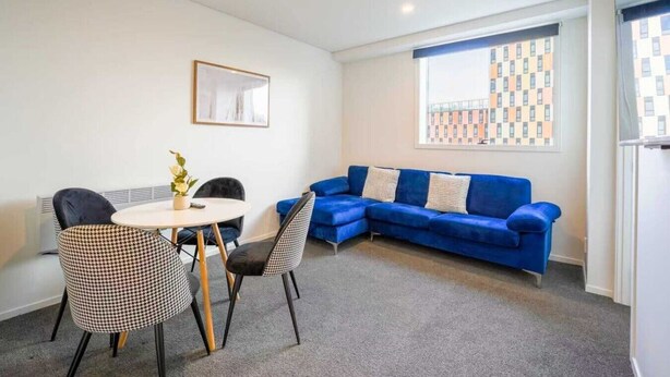 Een moderne woonkamer met een blauwe bank, hondentand patroon stoelen, een ronde tafel en een groot raam met uitzicht op de stad.