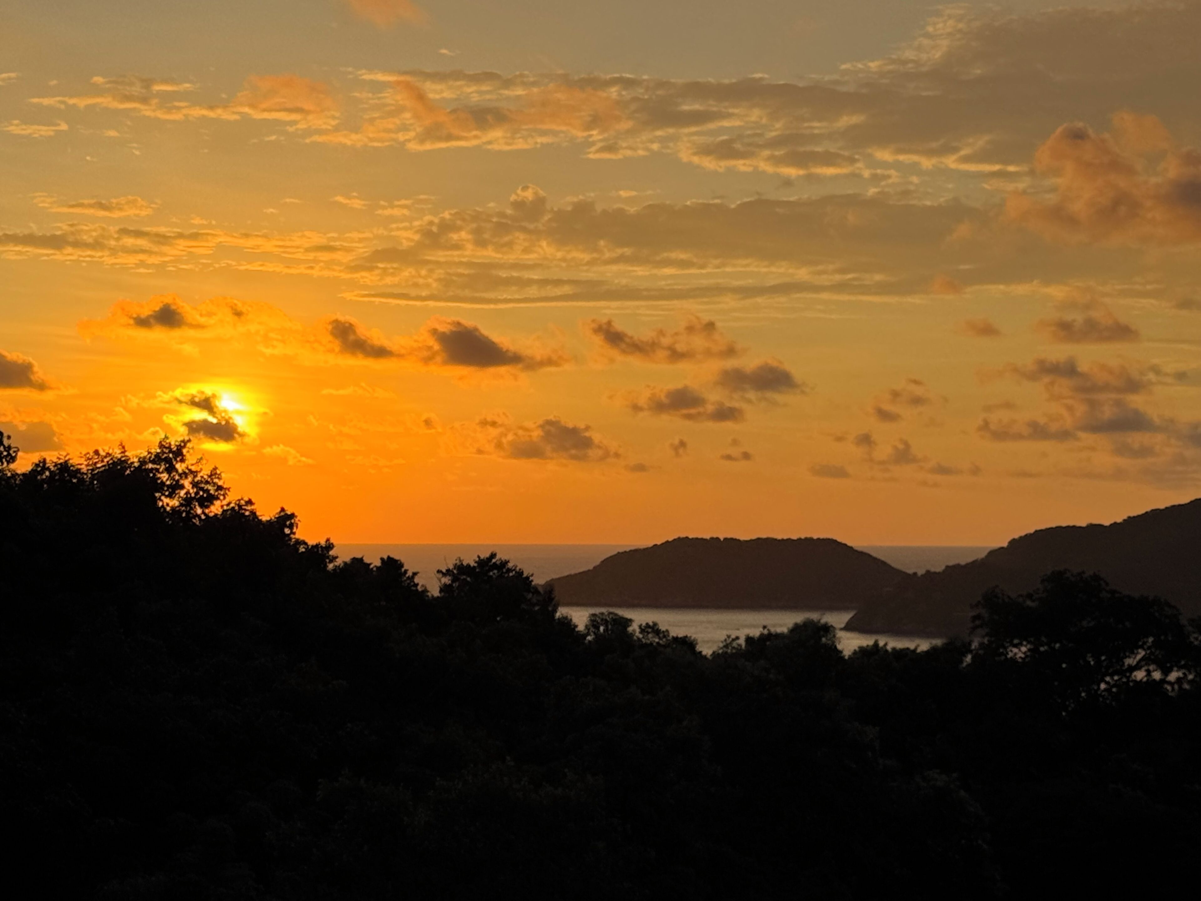 A sunset over a mountainous landscape with silhouettes of trees and hills.