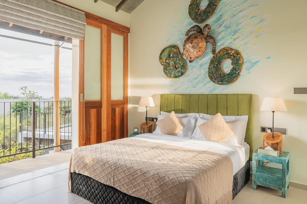 Une chambre avec un grand lit, une tête de lit verte, deux tables de chevet avec des lampes et un balcon avec vue.