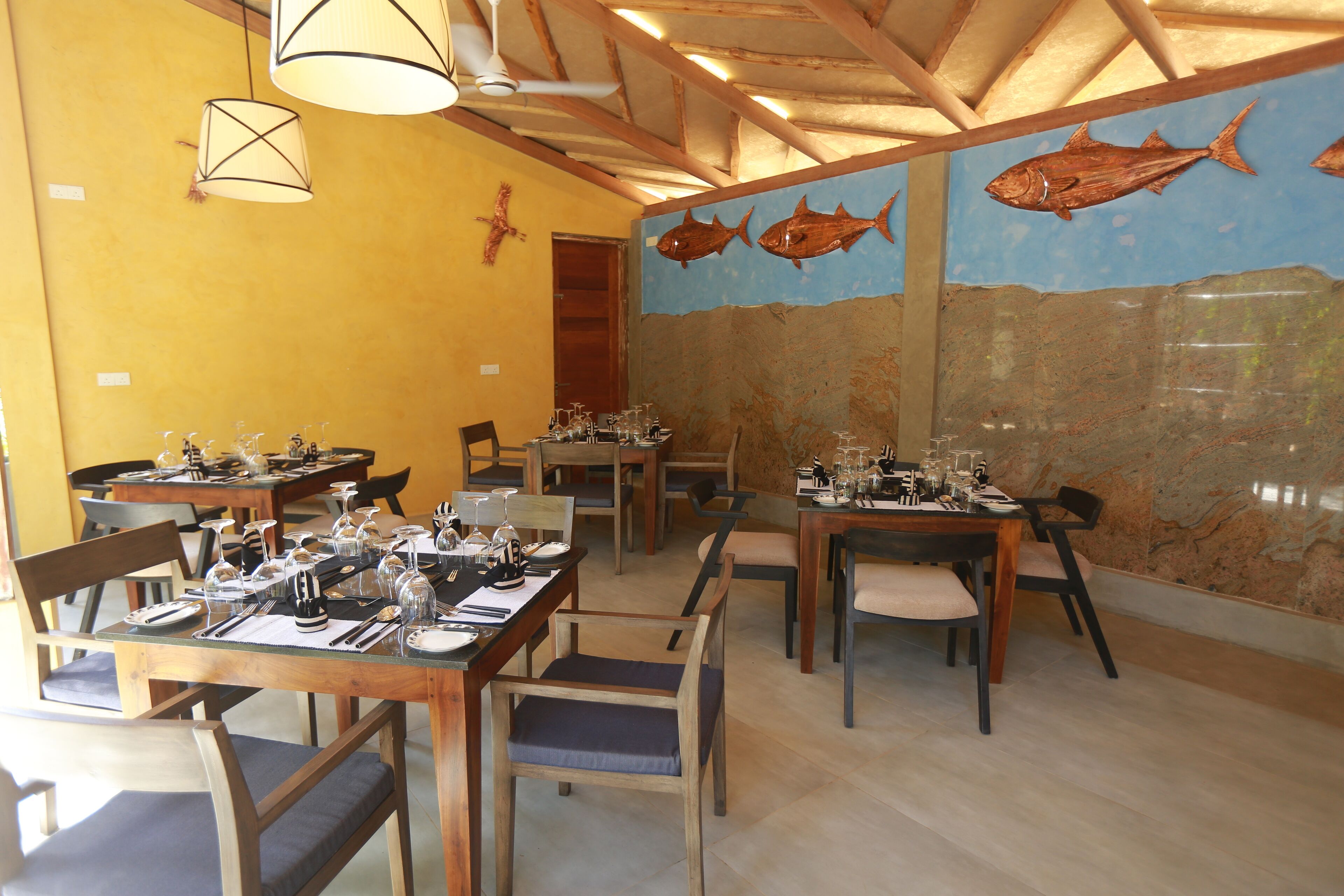 A restaurant with wooden tables and chairs, a mural of fish on the wall, and hanging pendant lights.