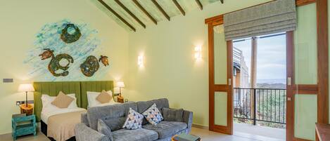 Quarto com cama, sofá, mesa pequena e varanda com vista.