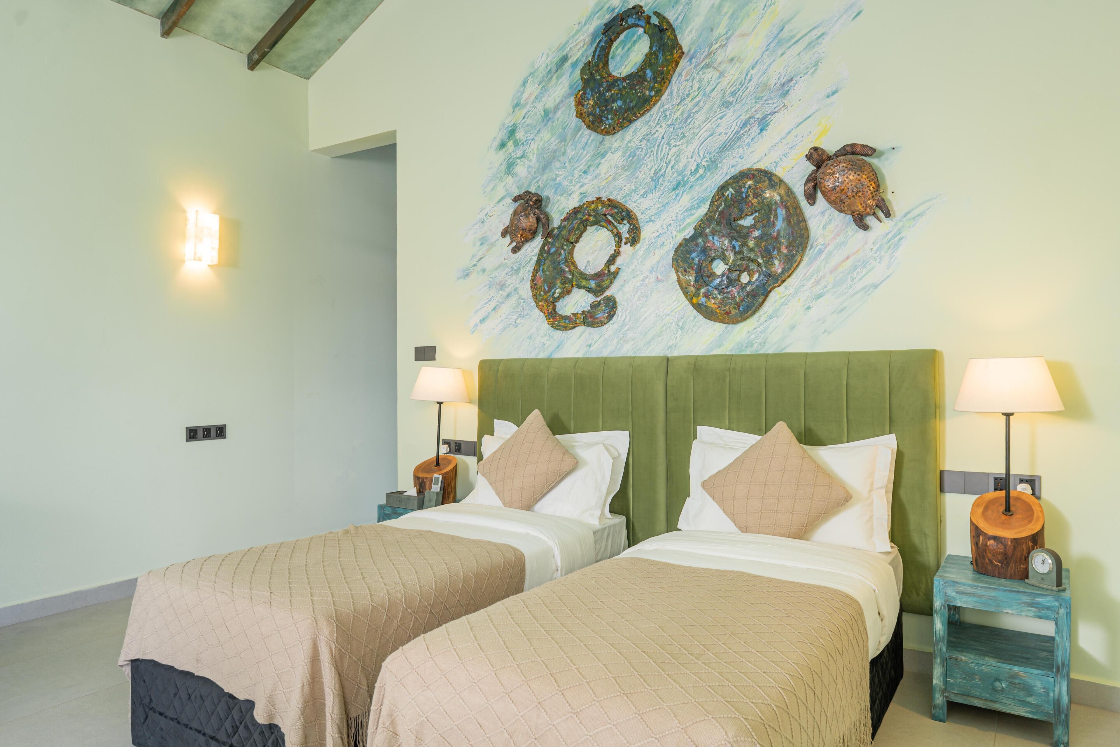A hotel room with two beds, a green headboard, and a wall mural of sea turtles.