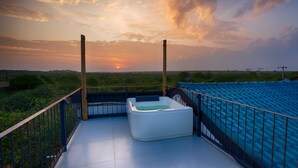 A balcony with a white bathtub, a railing, and a view of the sunset over a green landscape. - O2 Villas Yala (Yala)