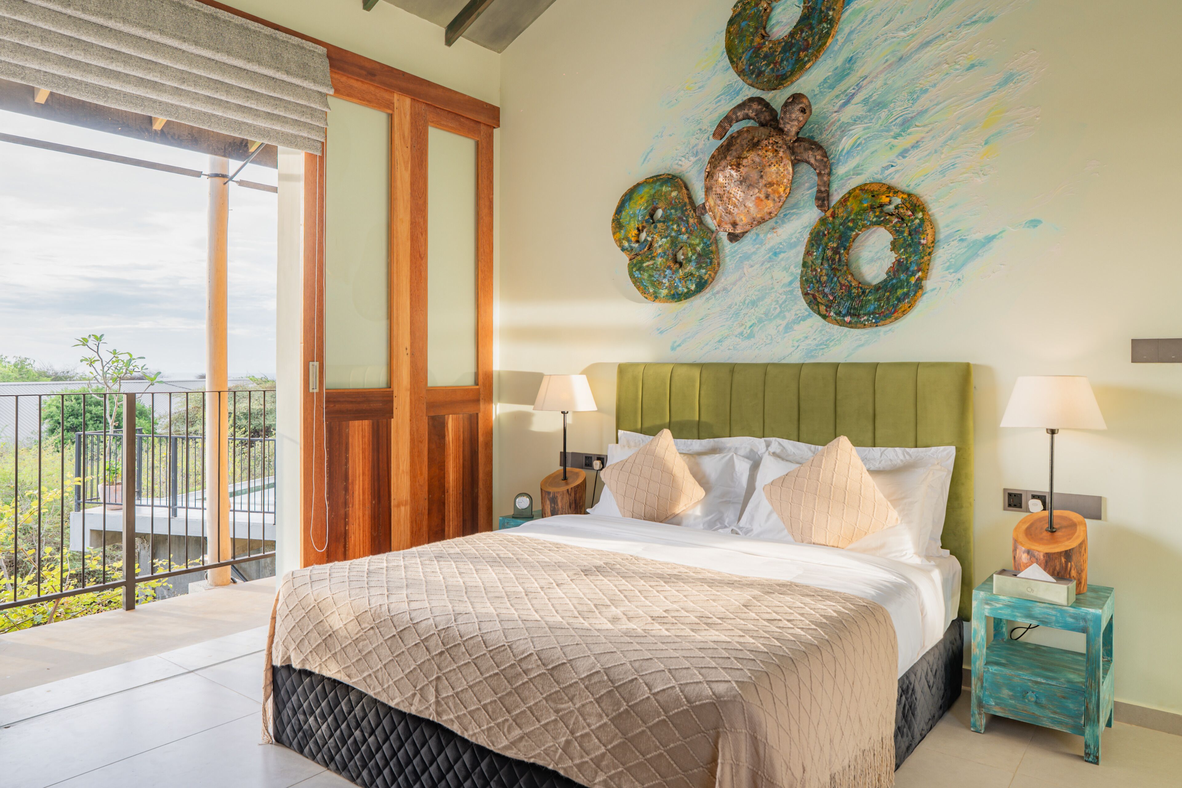 A bedroom with a bed, pillows, a nightstand, a lamp, a wall art piece, and a balcony with a view.