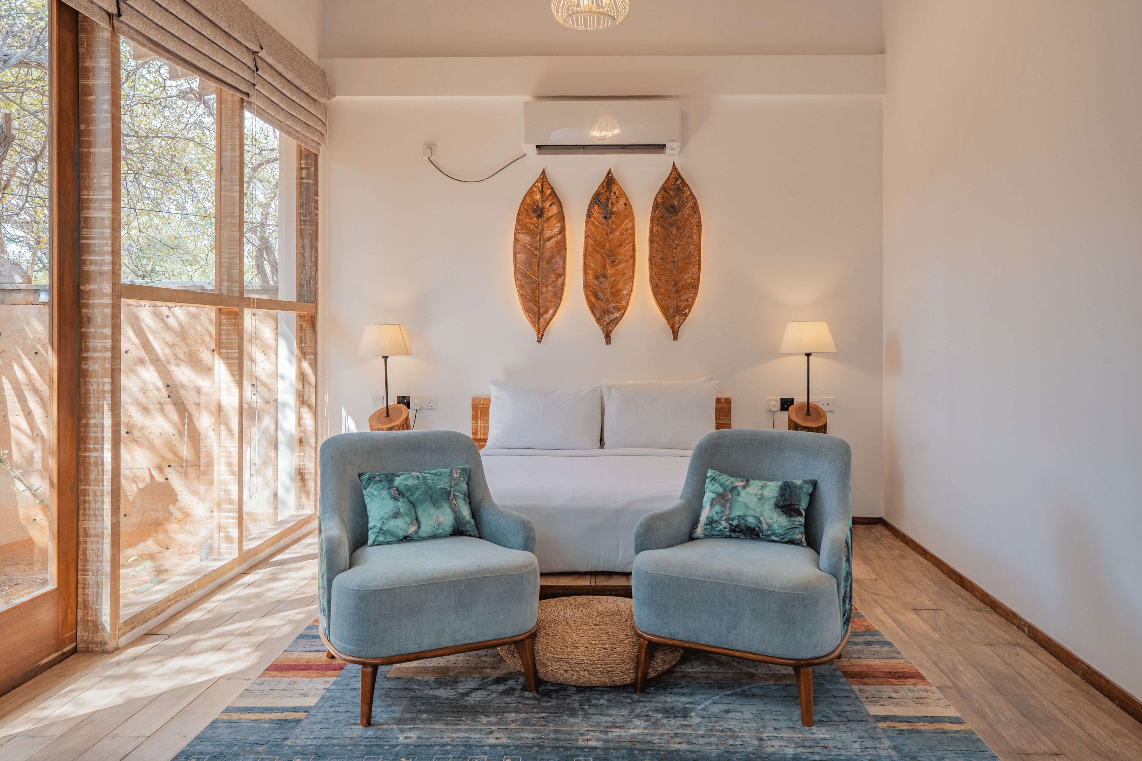 A bedroom with a large window, a bed, two armchairs, and wall-mounted decorative leaves.