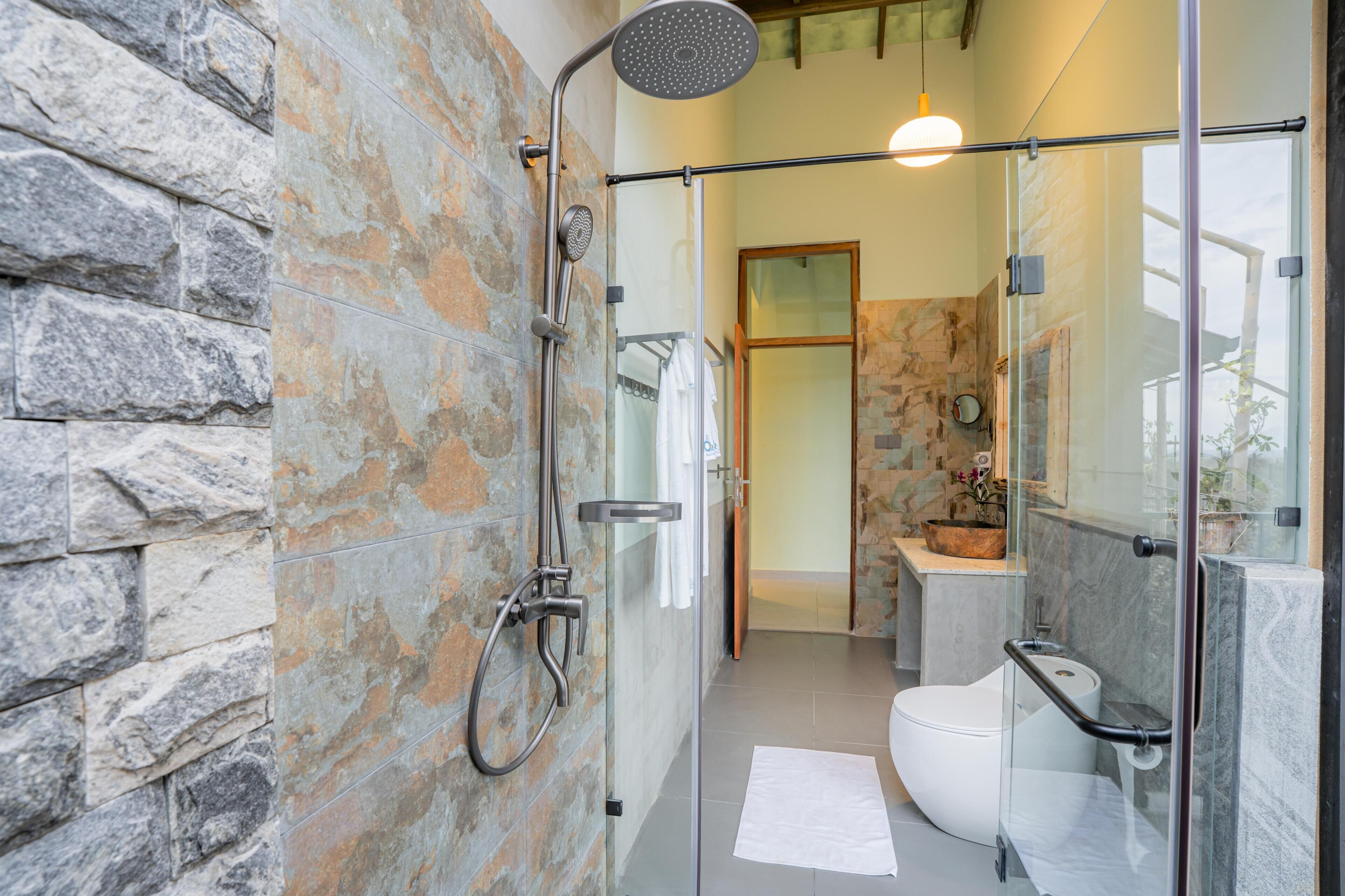 A modern bathroom with a glass shower enclosure, stone wall, and a white toilet.