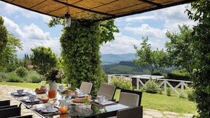 Een terras met een ontbijtgedekte tafel, omringd door groen en een prachtig uitzicht.