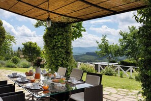 Un área de comedor al aire libre con una mesa lista para el desayuno, rodeada de follaje y vistas panorámicas.