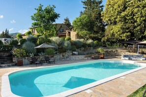 Una piscina con baldosas de piedra, rodeada por un muro de piedra y abundante vegetación.
