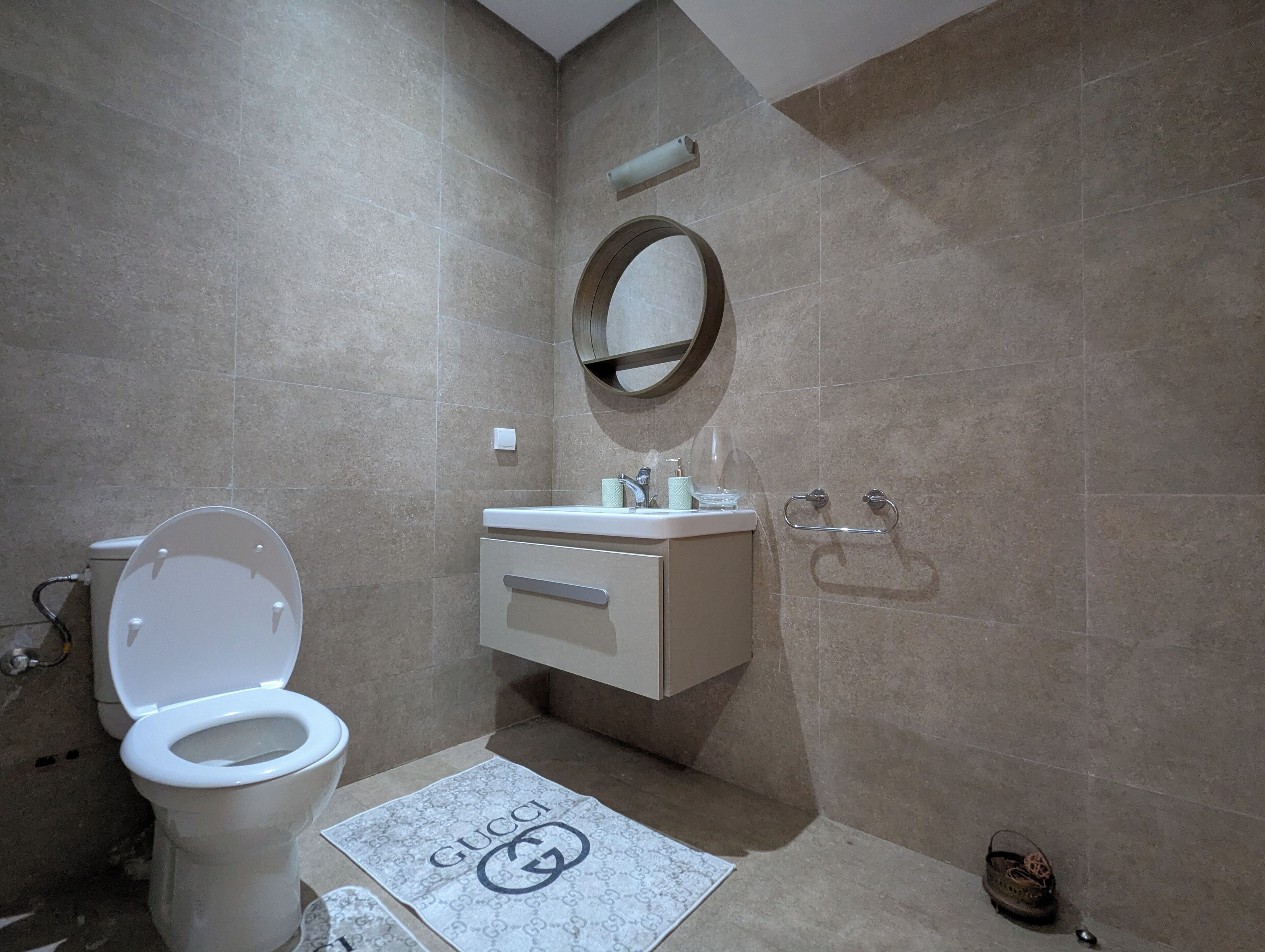 A bathroom with a toilet, sink, mirror, and towel mat.