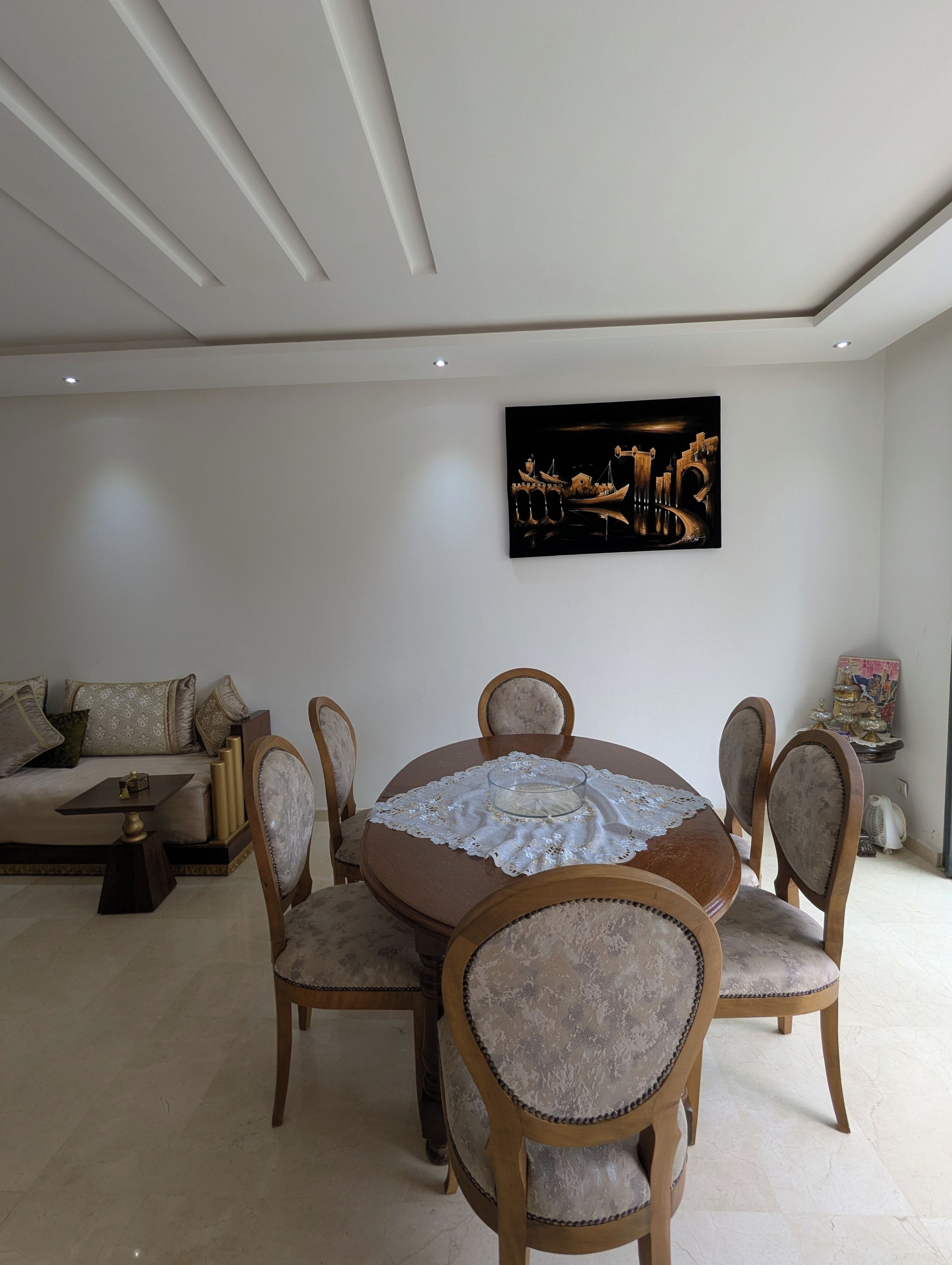 A dining area with a round table, six chairs, a sofa, and a painting on the wall.