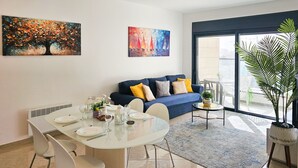 Un salon moderne avec un coin repas, comprenant un canapé bleu, une table à manger blanche et des œuvres d’art accrochées aux murs.