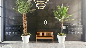 Un hall d’entrée moderne agrémenté de deux grands pots de plantes, d’un banc en bois et d’une boîte aux lettres fixée au mur.