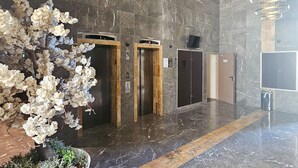 Un hall d’entrée avec un sol en marbre, trois ascenseurs et une grande composition florale artificielle.