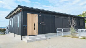 En moderne bygning med dør i træ, en metalport og et skilt med teksten "Oceanview Naruto".
