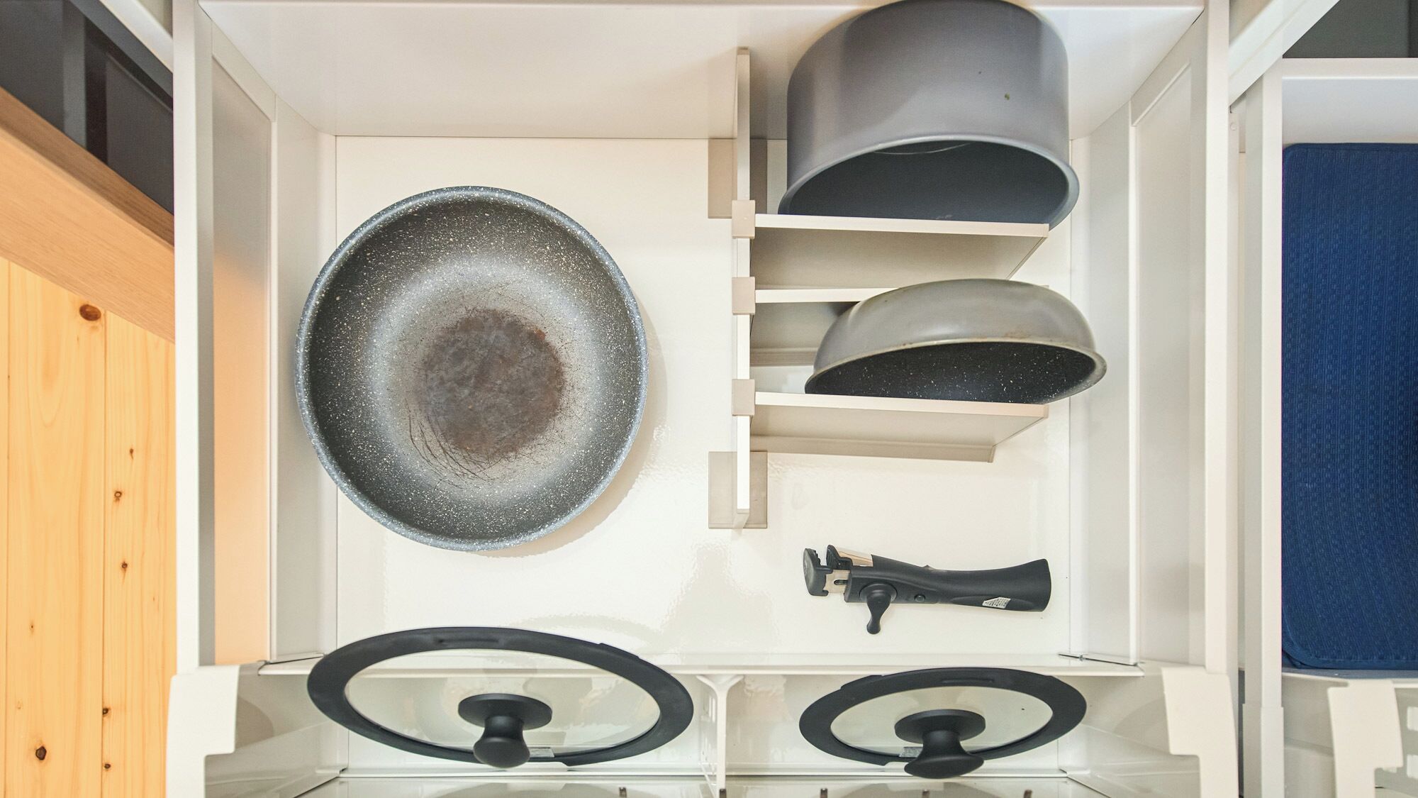 A kitchen with a large black frying pan, a stove with a black griddle, and a blue towel hanging on the wall.