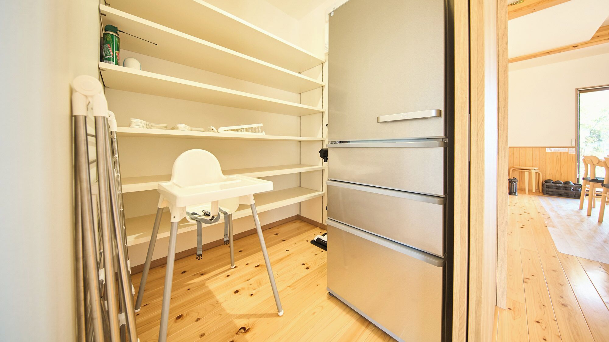 Una cocina compacta con refrigerador integrado, piso de madera y un estante alto con utensilios de cocina.