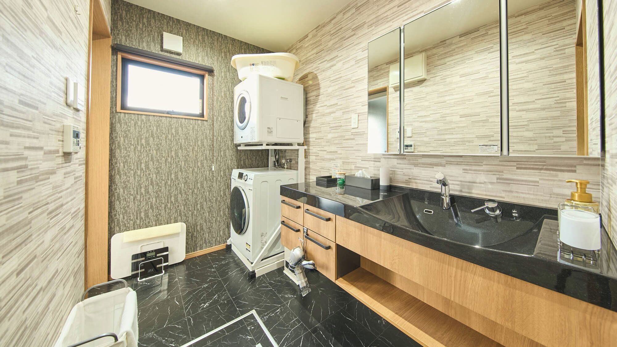 A modern bathroom with a black marble floor, a large sink, a mirror, and a washing machine.