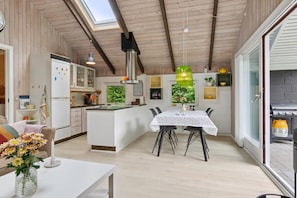 Une cuisine moderne dotée d’un îlot central, de poutres en bois au plafond et d’un coin repas avec une table et des chaises.