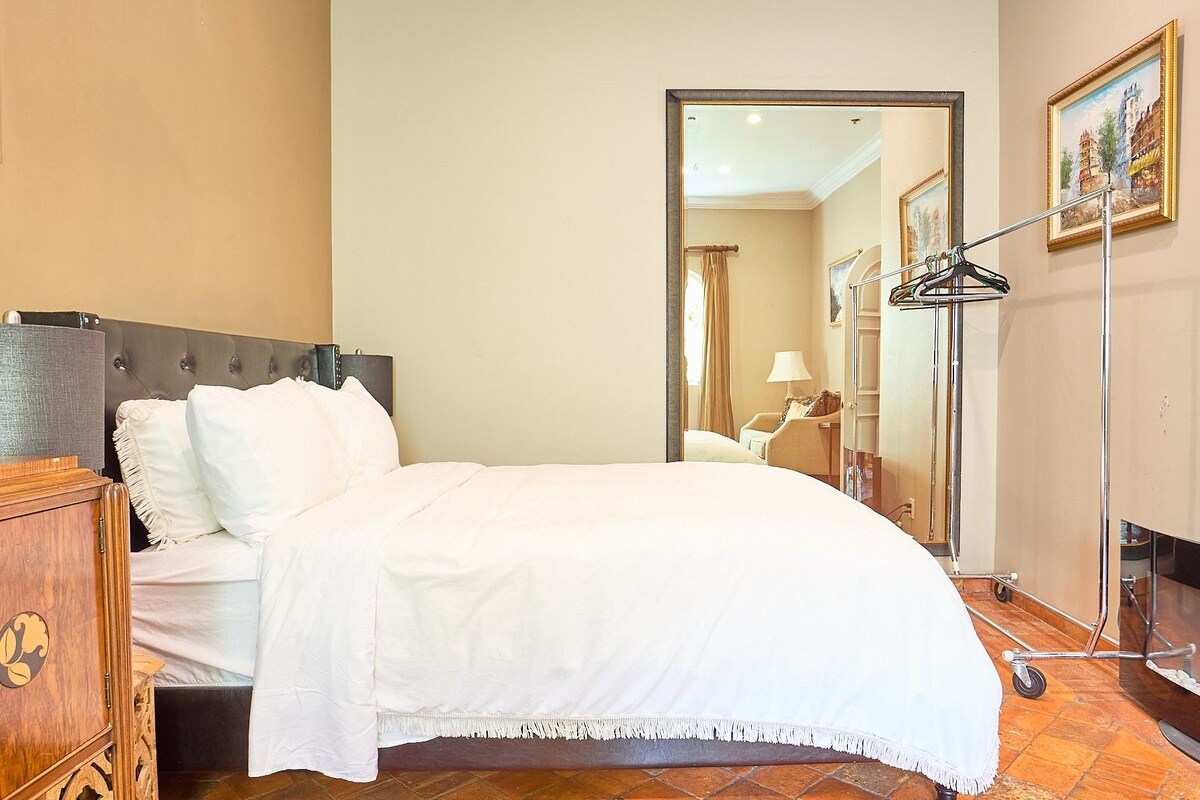 A hotel room with a bed, a wooden dresser, a mirror, and a painting on the wall.