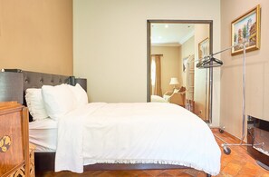 A hotel room with a bed, a wooden dresser, a mirror, and a painting on the wall. - Beverly Hills Spanish (Beverly Hills)