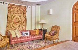 A living room with a pink sofa, a gold armchair, a patterned rug, and a large floral curtain. - Beverly Hills Spanish (Beverly Hills)