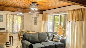 Uma sala de estar acolhedora, com teto de madeira, um sofá, uma mesa de centro e um espaço de jantar com mesa e cadeiras.