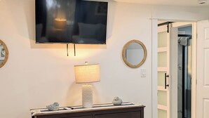 Quarto com cama, cômoda, televisão na parede, abajur e espelho.