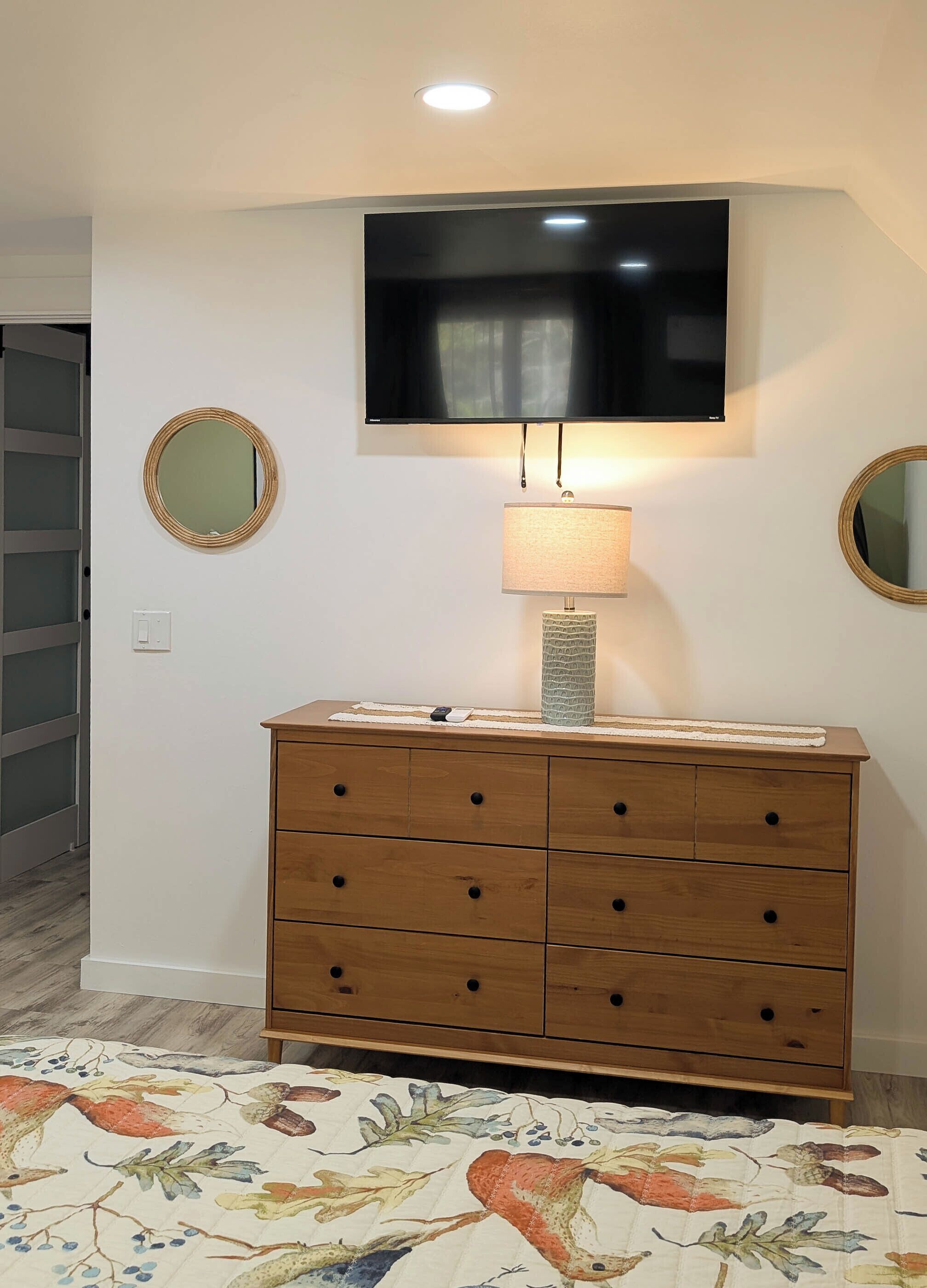 A room with a wooden dresser, a flat-screen TV mounted above it, and two round mirrors on the walls.