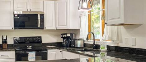 A modern kitchen with white cabinets, a black stove, and a granite countertop.