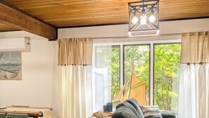 Uma sala de estar acolhedora com teto de madeira, área de jantar com mesa e cadeiras, e uma grande janela com cortinas.