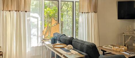 A modern living room with a black sofa, wooden ceiling, and a large window with curtains.