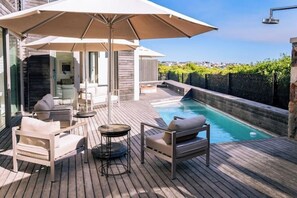 Ein Poolbereich auf dem Dach mit Liegestühlen und Sonnenschirm, umgeben von einer Holzterrasse und Blick auf die Stadt.