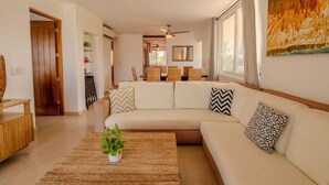 Una sala de estar moderna con un sofá modular, una mesa de centro con una planta y un ventanal con cortinas.