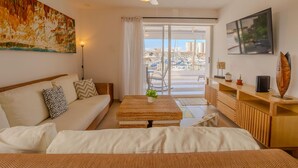 Una habitación de hotel moderna con sofá, una mesita de centro de madera, televisión y balcón con vistas a la ciudad.