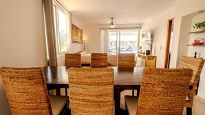 Un comedor con una mesa de madera y sillas tejidas, un ventanal con cortinas y vistas a la ciudad.