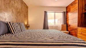 Un dormitorio con una cama grande, un armario de madera, un ventanal con cortinas y una pared con textura.