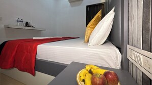 Una habitación de hotel con una cama, una mesita de noche con frutero, una colcha roja y un aire acondicionado de pared.