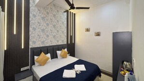 Habitación de hotel con cama, ventilador de techo, mesita de noche y pared con estampado floral.