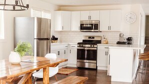 A modern kitchen with white cabinets, stainless steel appliances, and a wooden dining table with benches. - Rustic Lake Nokomis Cabin with Hot Tub, Trails, and Family Fun for 10! (Tomahawk)