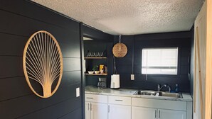 A modern kitchen with dark walls, white cabinets, a hanging light fixture, and a window with blinds.