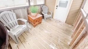 A covered porch with two Adirondack chairs, a wooden table with a plant, and a door. - Rustic Lake Nokomis 2BD/1Bath Lakeside Cabin - Cabin #3 (Tomahawk)