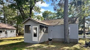 A small, single-story cabin with a door and a window, surrounded by trees and a grassy yard. - Rustic Lake Nokomis 2BD/1Bath Lakeside Cabin - Cabin #3 (Tomahawk)